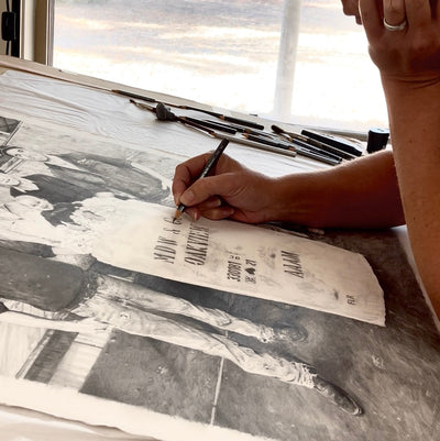 Jaime Prosser in her studio drawing with the light from the window behind her shinning in.